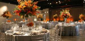 An elegant indoor event setup with round tables adorned with crystal-clear chairs, fine tableware, and large floral arrangements, ideal for formal occasions and indoor event rentals.